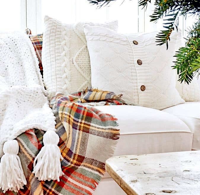 Cozy home decor white pillows with plaid blanket and tassles in sunroom.