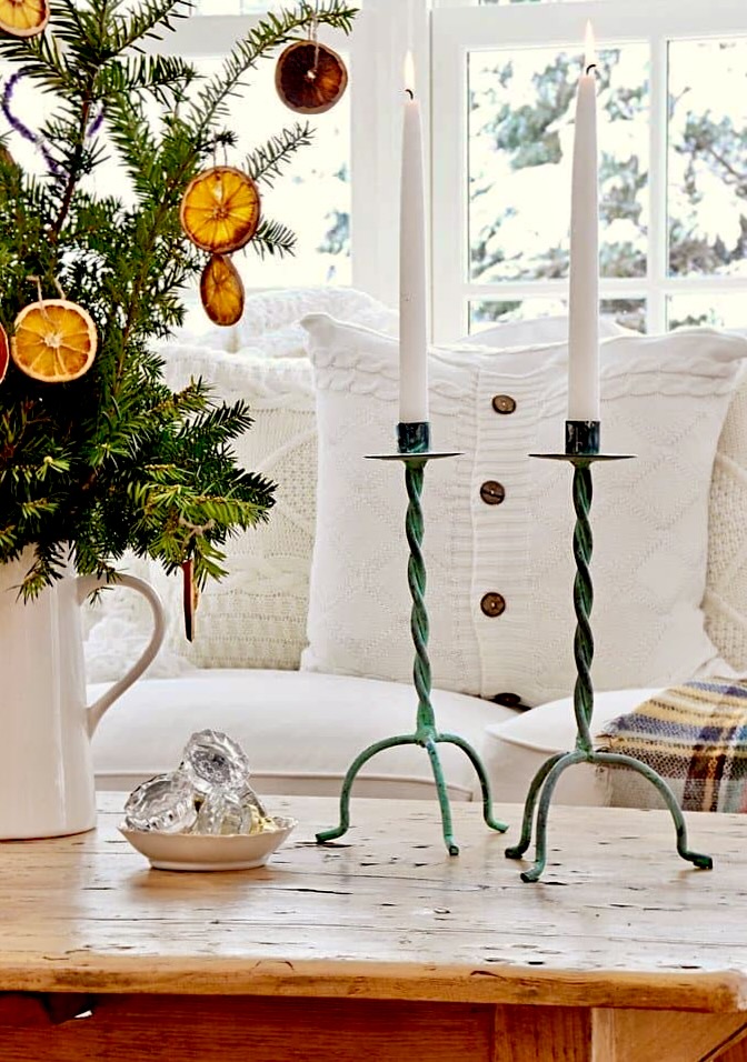 Two Patina candlesticks in cozy home decor with pillows on Christmas styled coffee table.