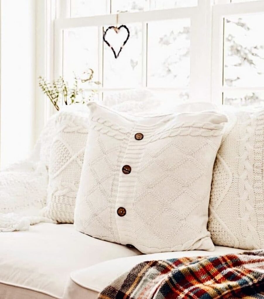 Cozy home decor white pillows on sofa with plaid blanket and purple heart hanging in the window.