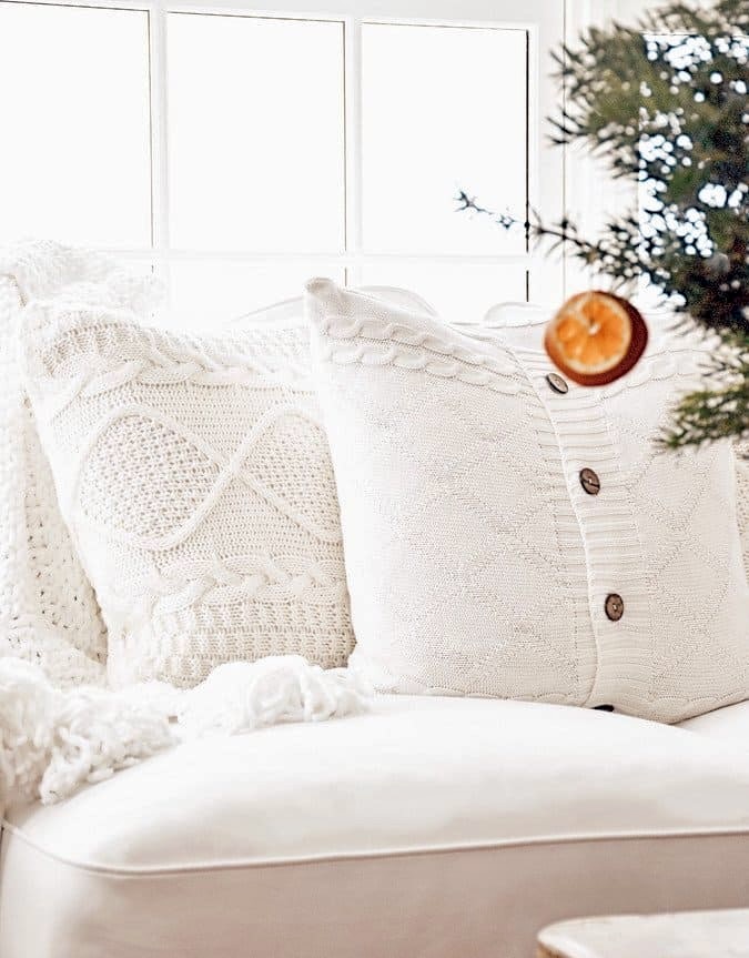 Cozy home decor in winter white with pillows and orange hanging from evergreen Christmas tree.