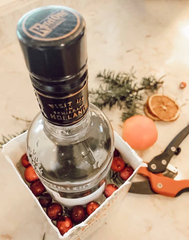 Bottle of alcohol in cut carton with berries and water.