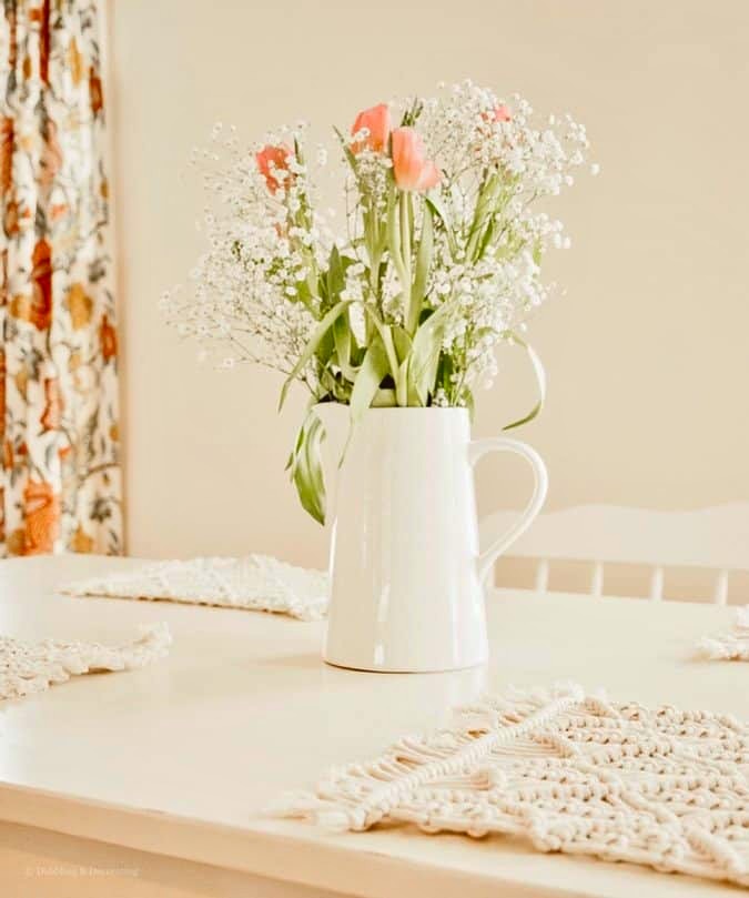 White pitcher with pink tulips on white dining room table next to Sherwin Williams Navajo White wall.