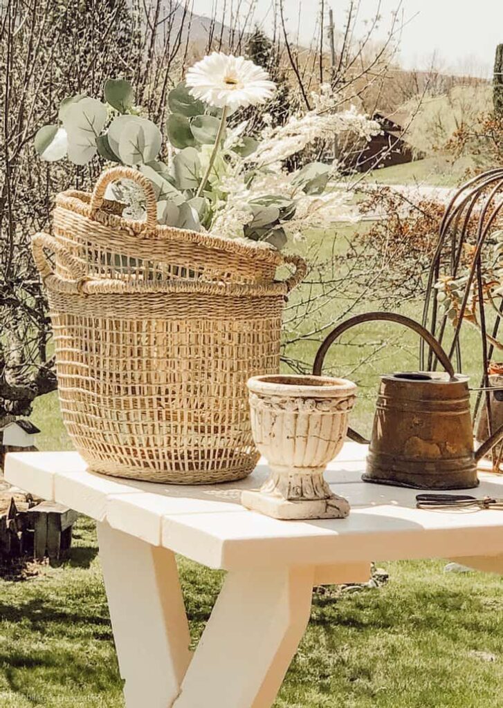 Baskets, urn, and watering can on white garden table close up outdoors.