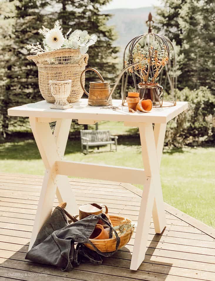 White DIY garden table outdoors with baskets, terracotta pots, urns and watering can.