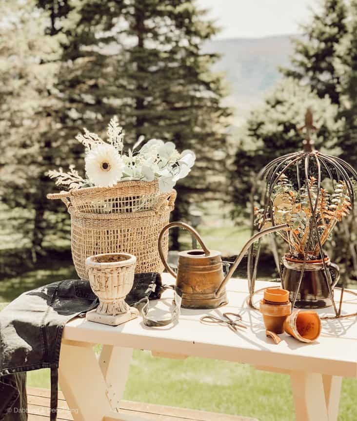 Baskets, urn, and watering can on white garden table close up outdoors.