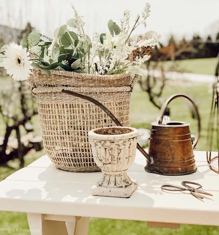 DIY garden table painted and decorated with baskets, urn, watering can and scissors outdoors.