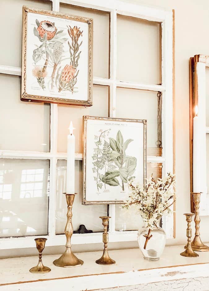 botanical prints framed hanging on salvaged window over vintage fireplace mantel with brass candleholders.