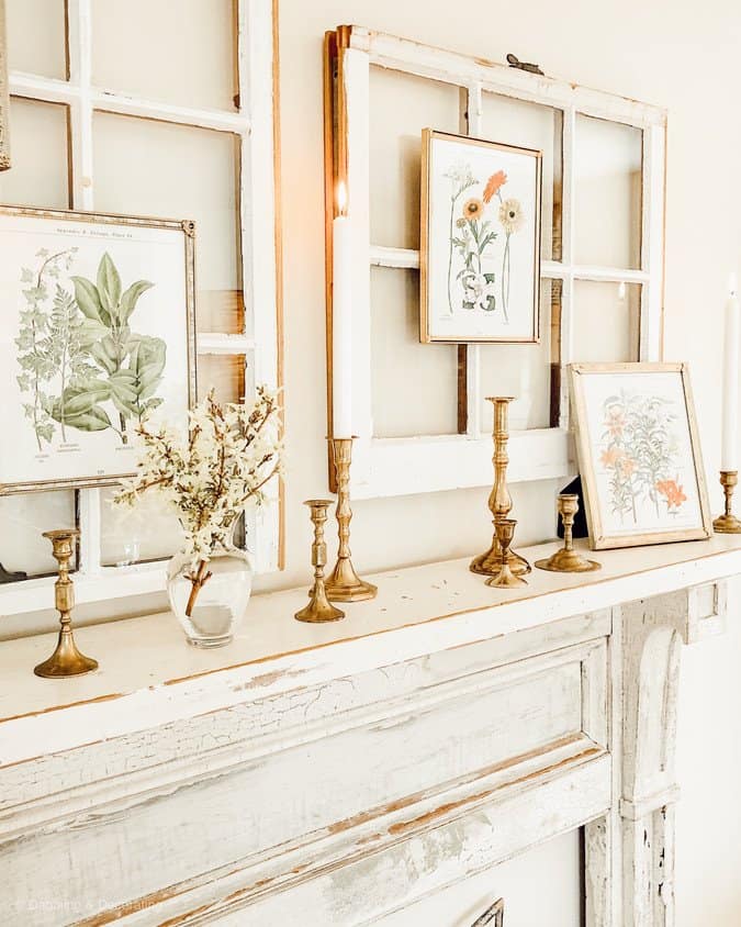 botanical prints framed hanging on salvaged window over vintage fireplace mantel with brass candleholders.