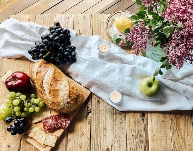 Picnic set up with breadboard and fruits on picnic table.