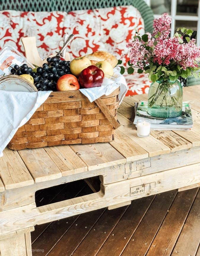 Vintage picnic basket filled with fresh fruits on pallet coffee table on porch.