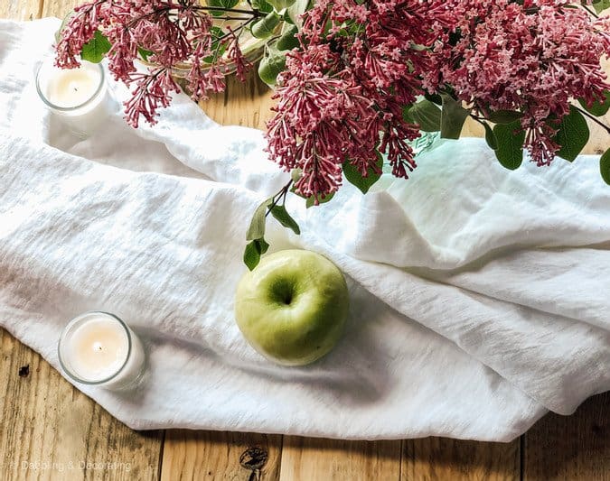 White linen tablecloth on pallet coffee table with green apple and flowers.