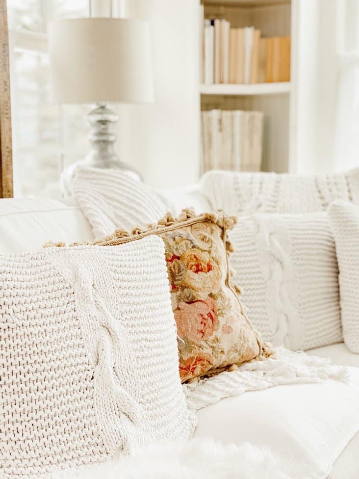 Winter white pillows with one colored embroidered pillow on all white couch.