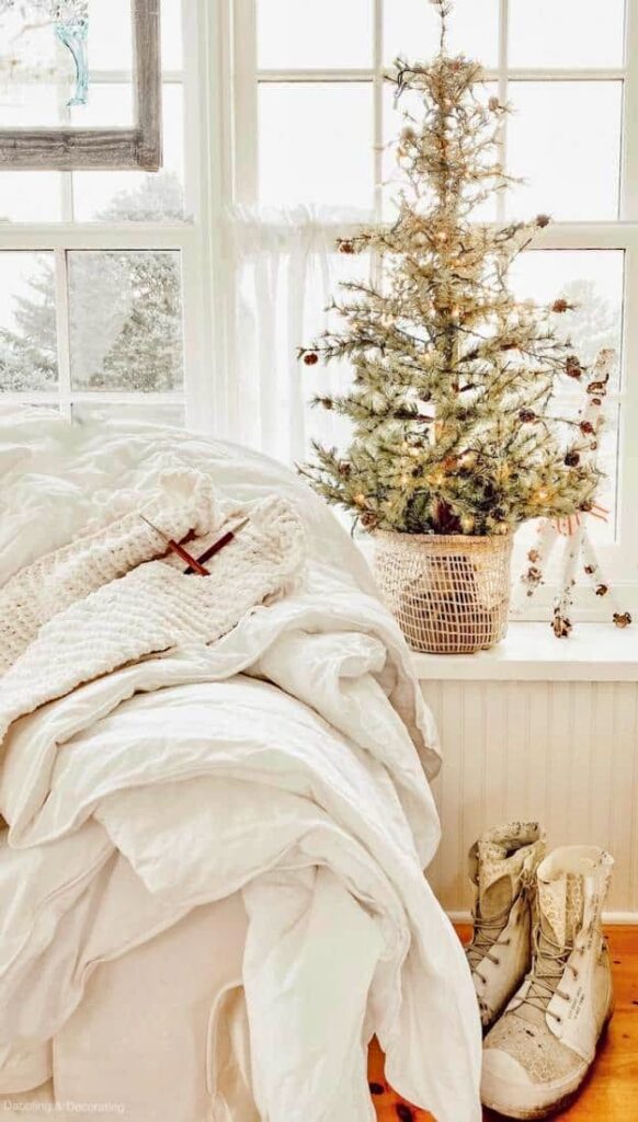 Winter white decorations in cozy sunroom with vintage snow white snow boots and Christmas tree in window.