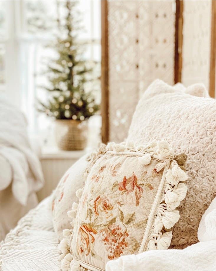 Cozy winter white decorations in sunroom with embroidery pillows and small window Christmas tree.