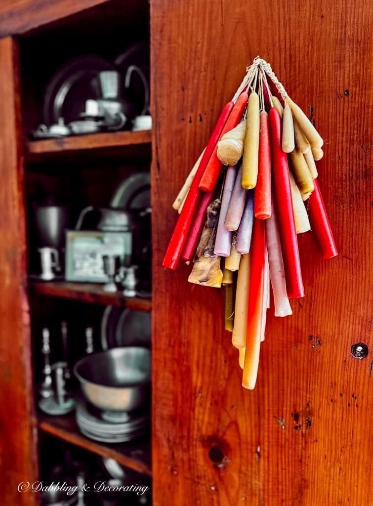 Antique Pewter Collection in vintage hutch with stacks of candles hanging on open door.