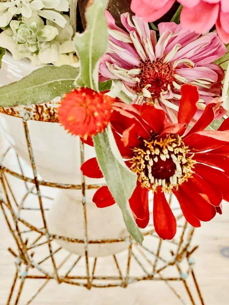 Red and pink flowers in stoneware inside wire basket centerpiece.