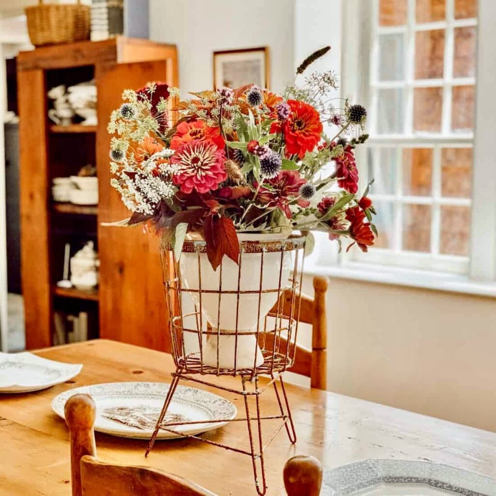 Vintage centerpiece in wire basket with colorful florals on antique table.