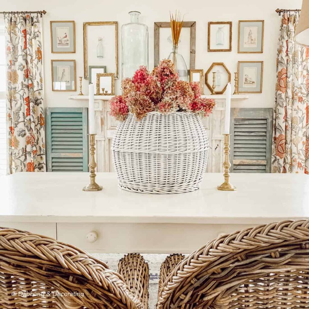 Vintage white basket with pink hydrangeas on dining room table in front of gallery wall of frames.