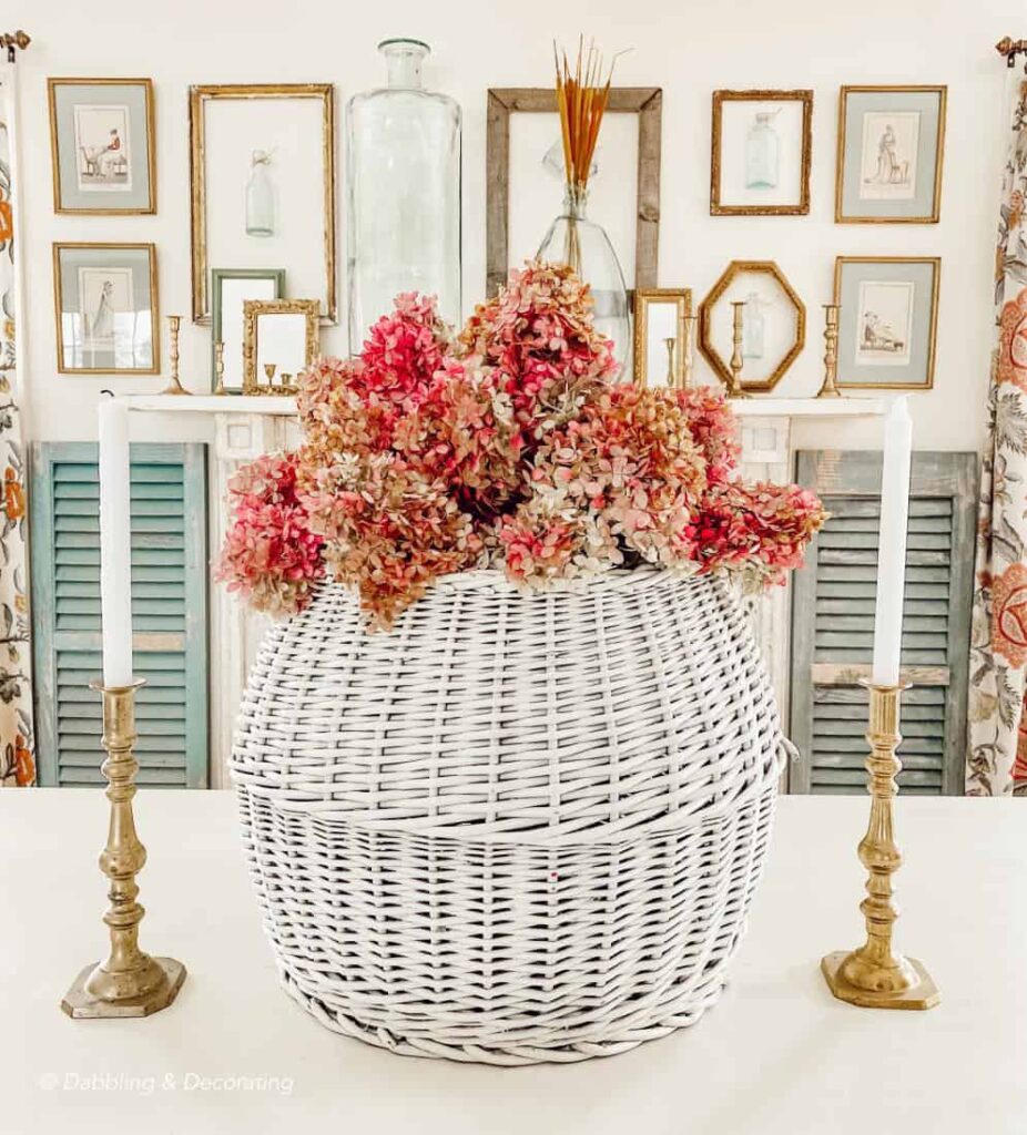 White basket with pink hydrangeas on dining room table in front of gallery wall of gold frames.