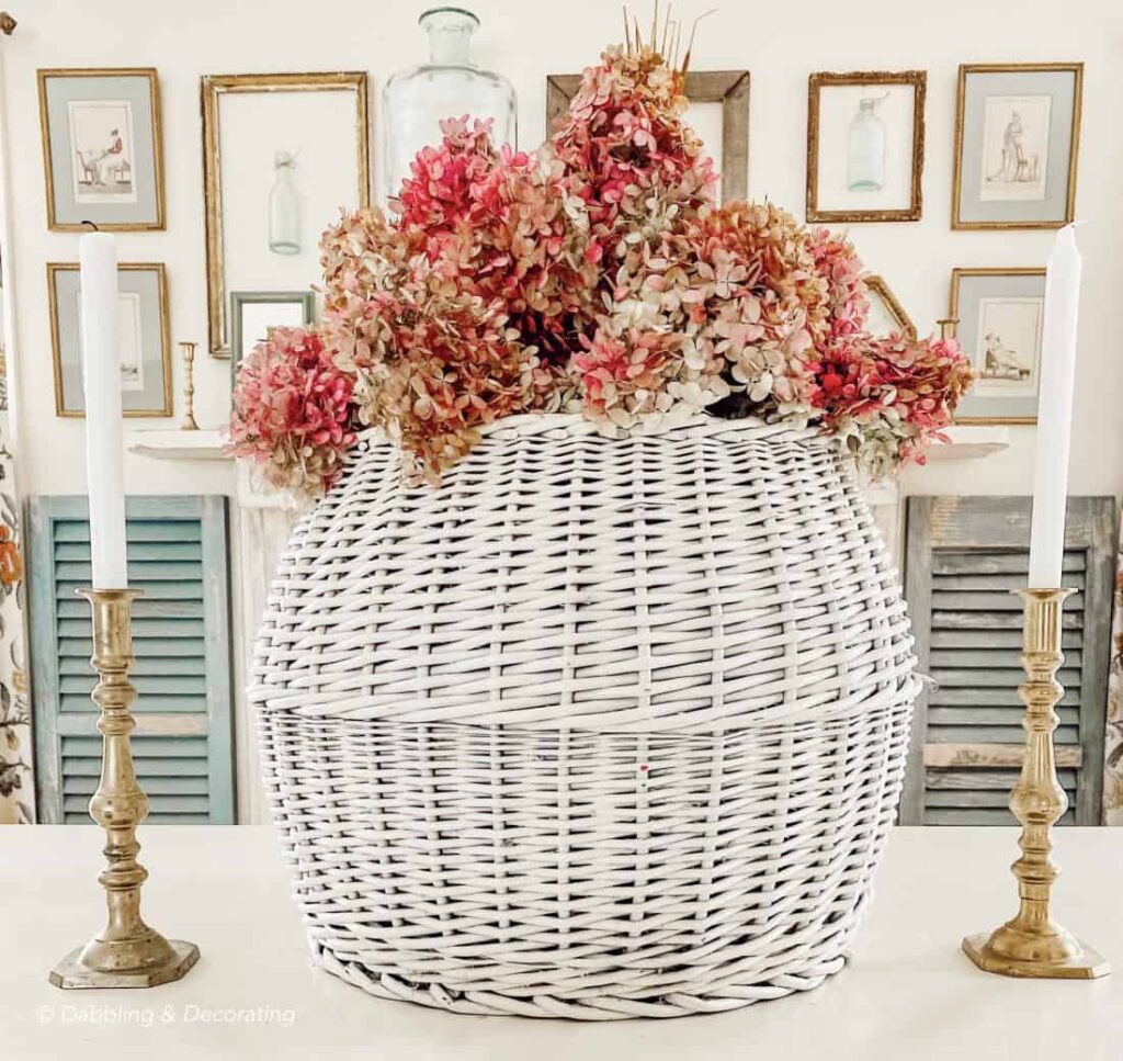 White basket with pink hydrangeas centerpiece on table with brass candlesticks.