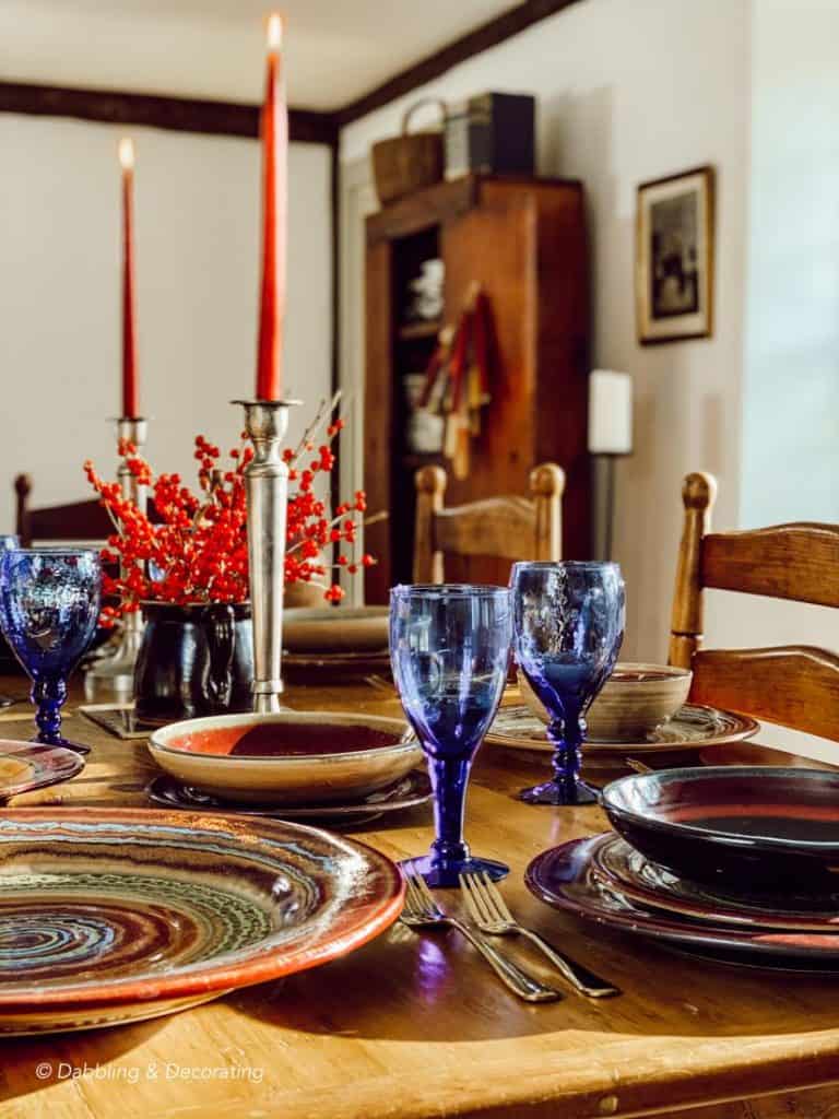 A vintage table setting with blue and red plates and glasses, decorated in a thrifty manner.