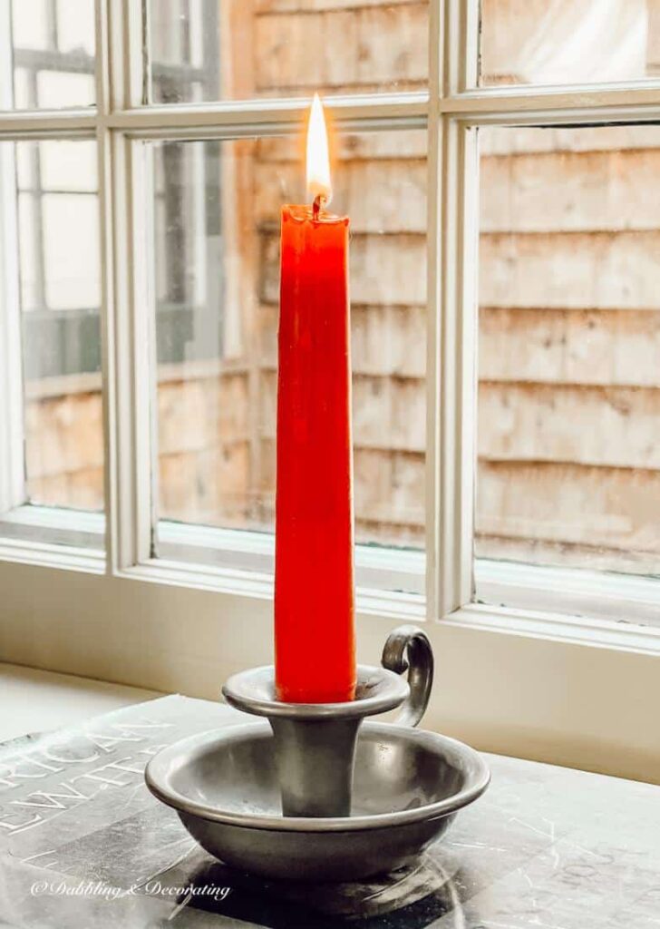 Lit red candle and pewter candlestick on vintage book on windowsill decor.