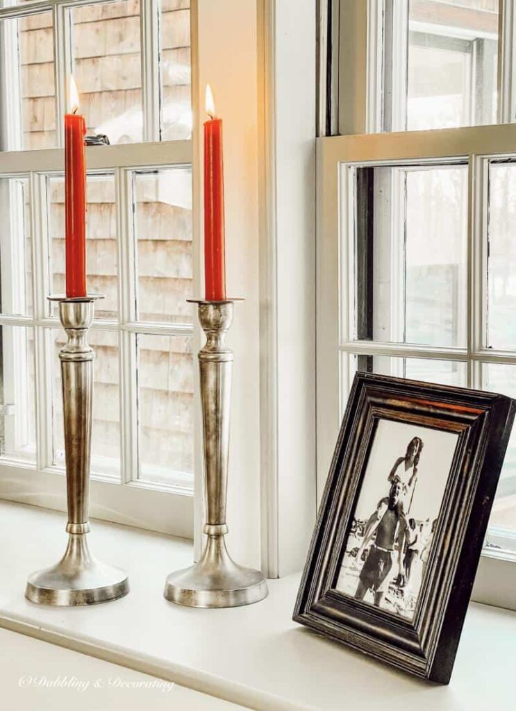 Pewter candlesticks with red tapered candles and framed photograph in windowsill decor.