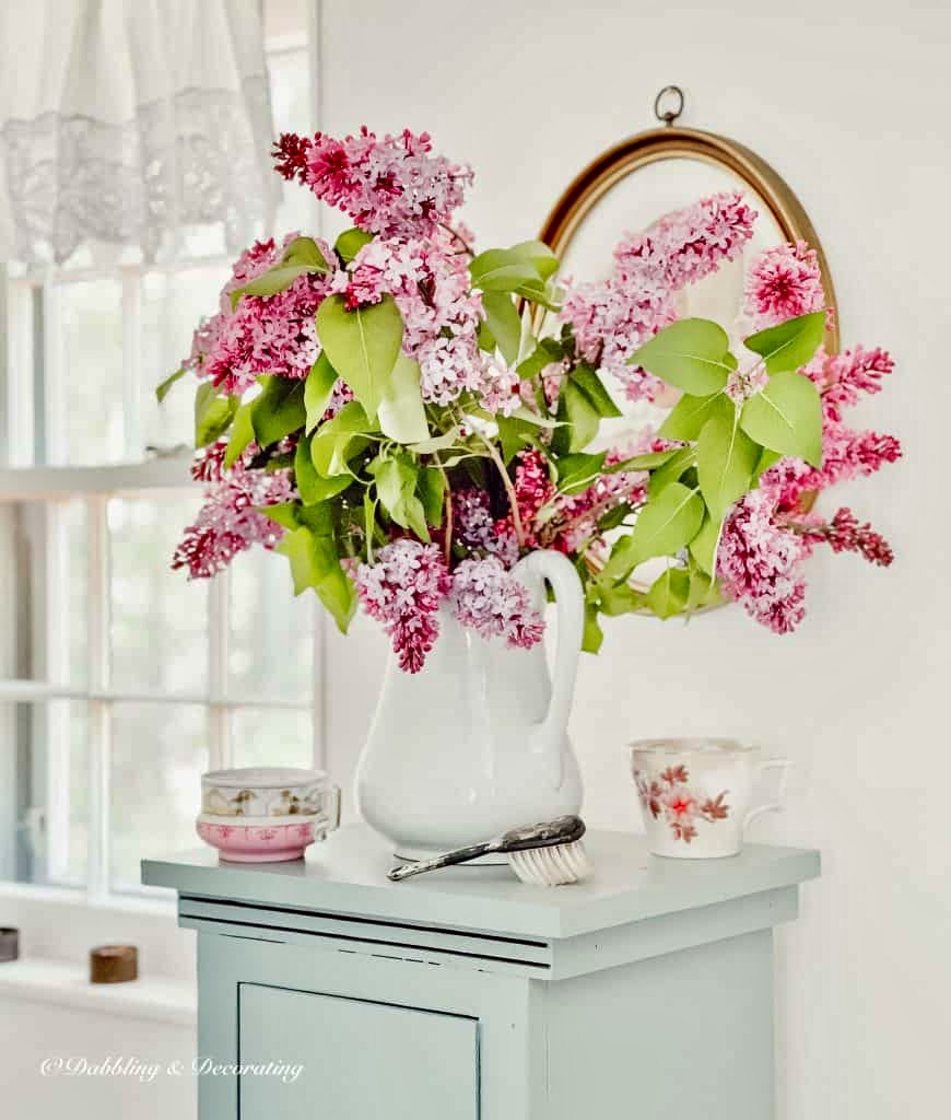 Purple Lilac bouquet in white pitcher in bathroom.