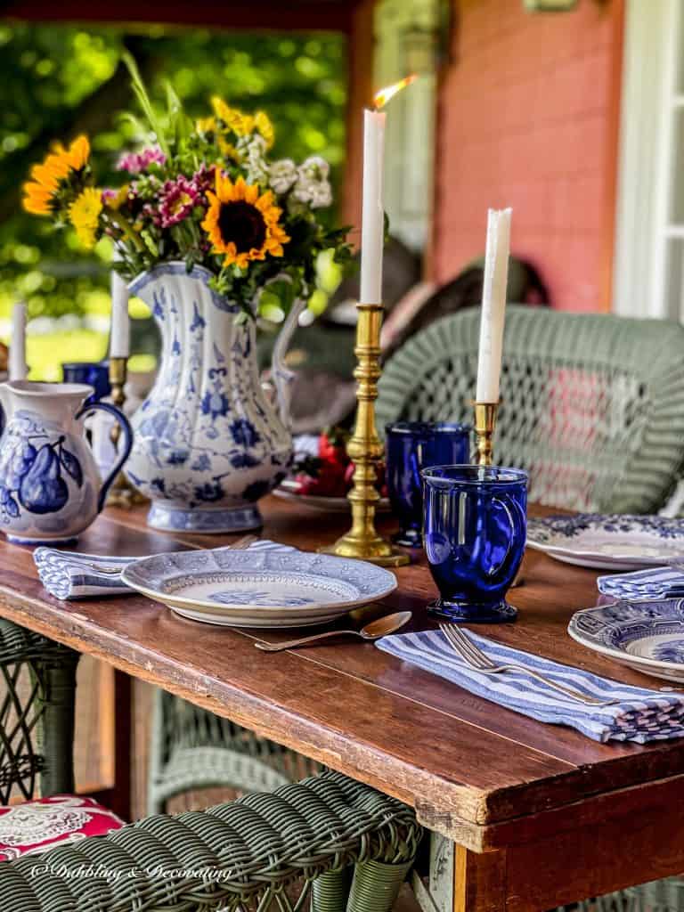 Vintage wooden table with blue and white table setting on outdoor porch.