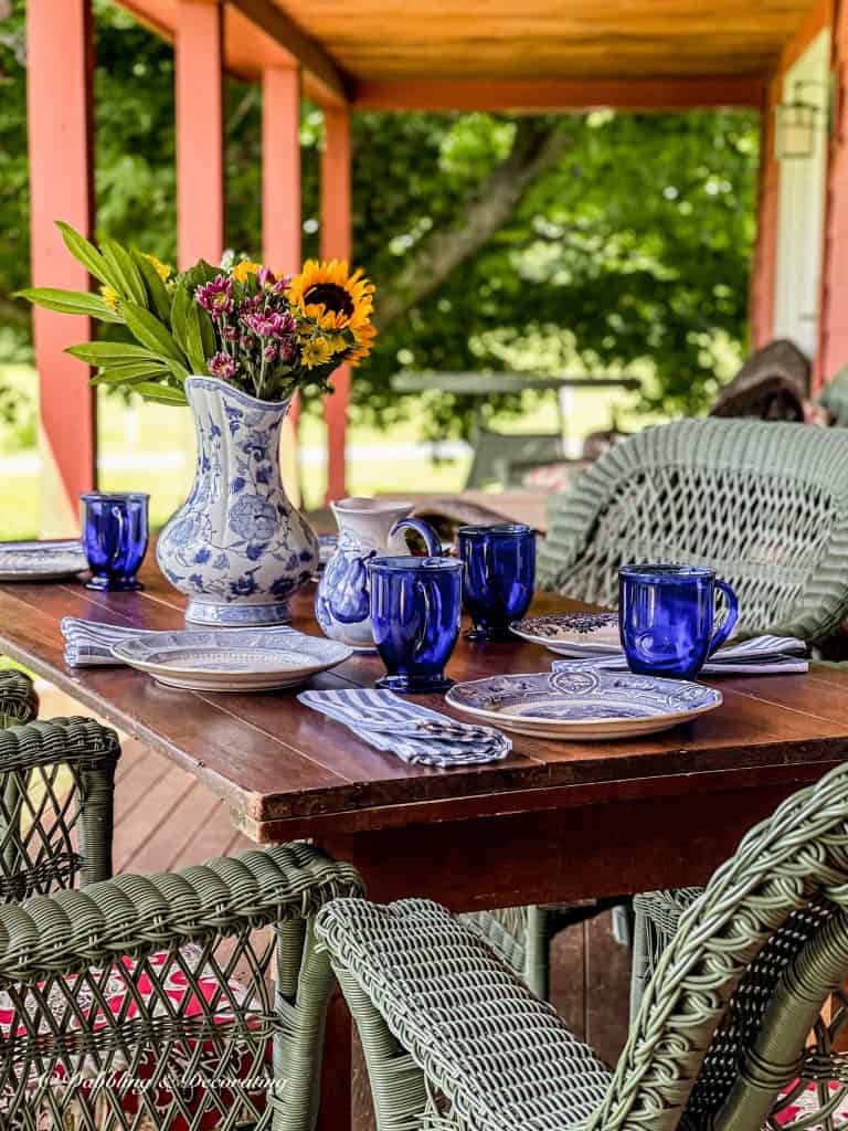 Vintage wooden table with blue and table setting on outdoor red porch.