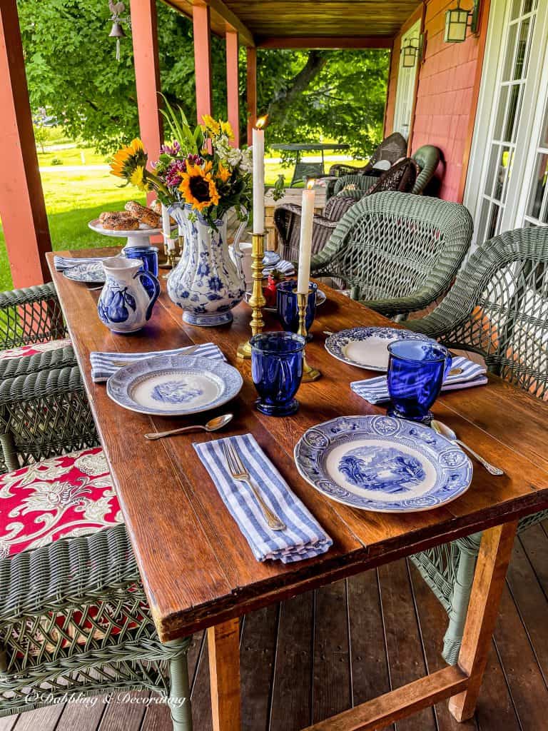 Outdoor porch table with blue and white table setting on outdoor red porch.