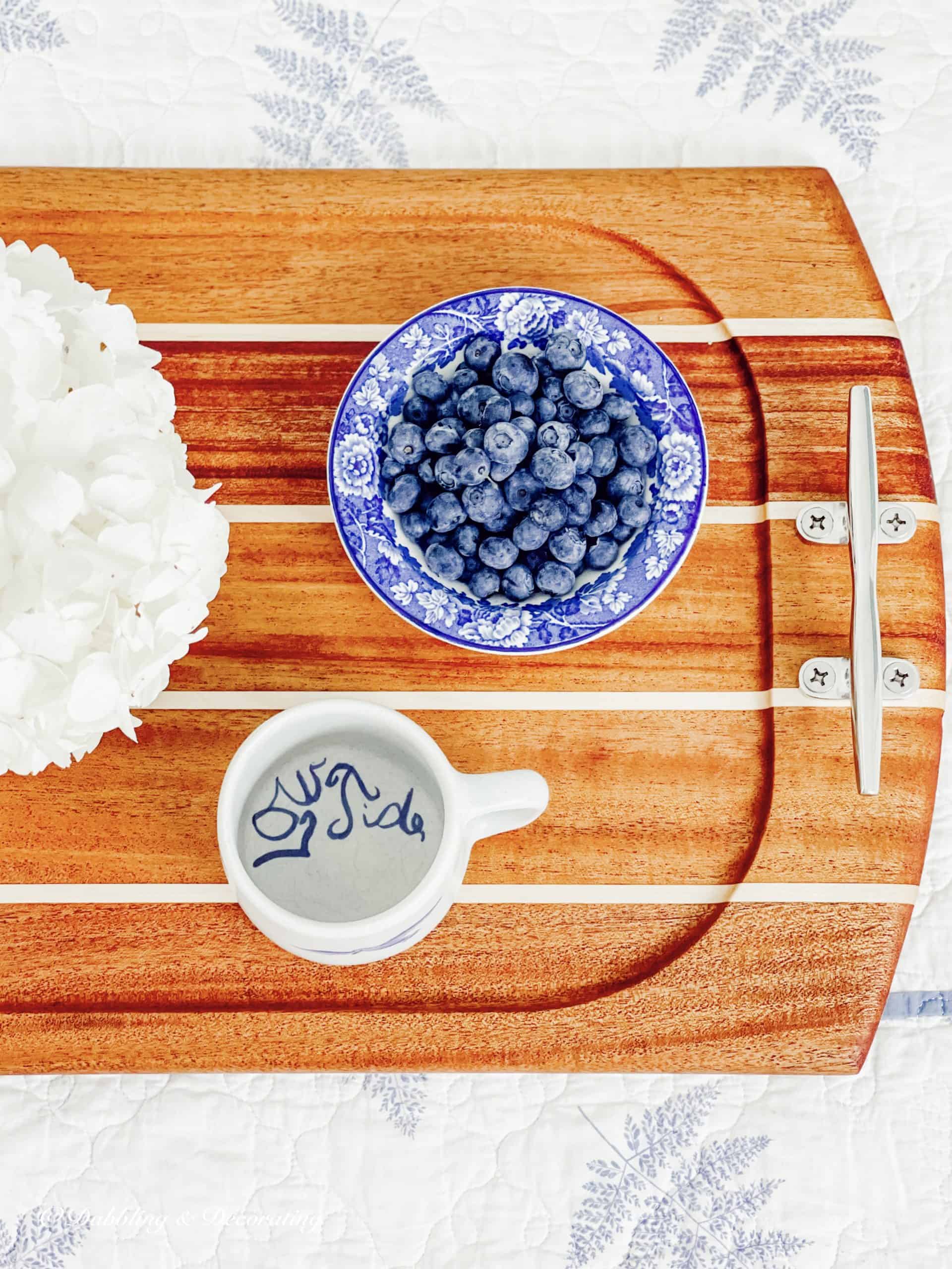 A vintage wooden serving tray adorned with a delightful arrangement of blueberries and accompanied by a dainty cup.