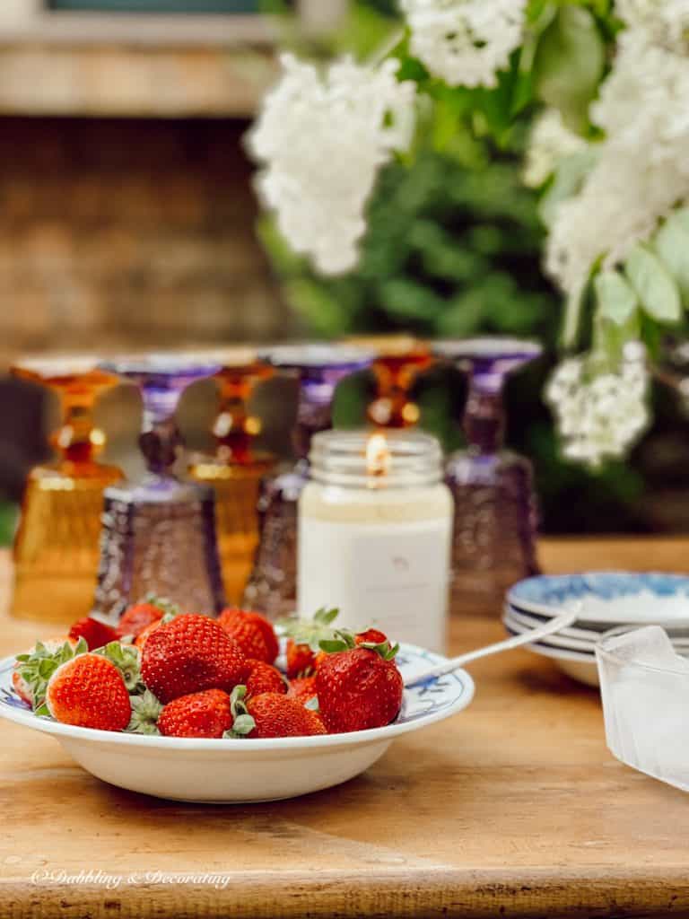Bowl of strawberries, candle and vintage glassware on outdoor beverage table.