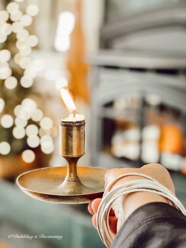 Vintage brass candlestick with lit candle in hand next to ski lodge fireplace.