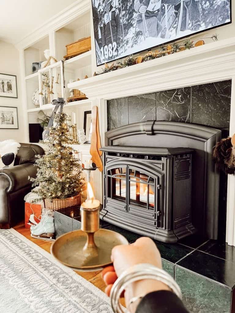 Vintage brass candlestick in hand lit in front of ski lodge fireplace with ski movie on TV.