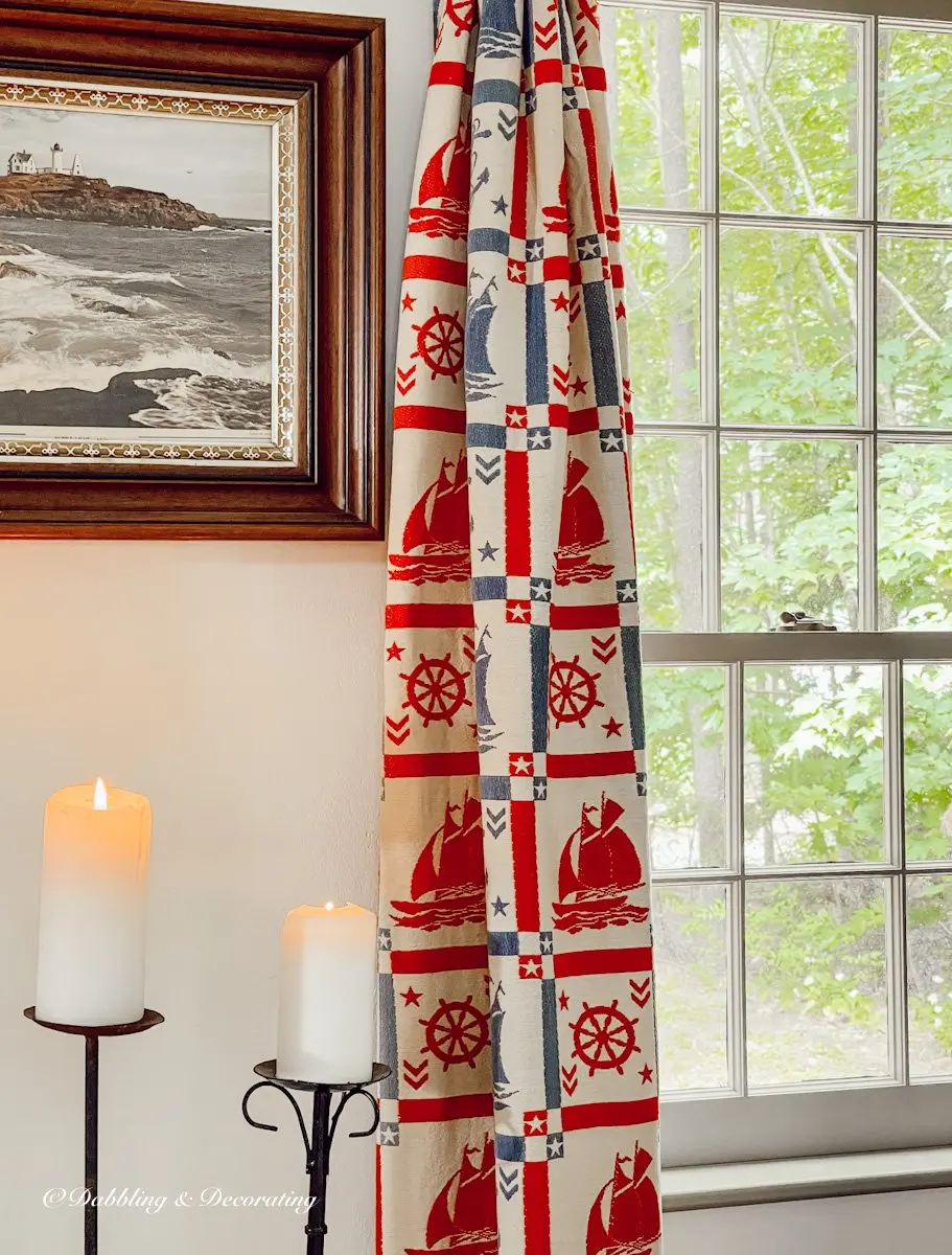 Red and Blue Coastal Curtains on window next to Lighthouse picture and burning candles.