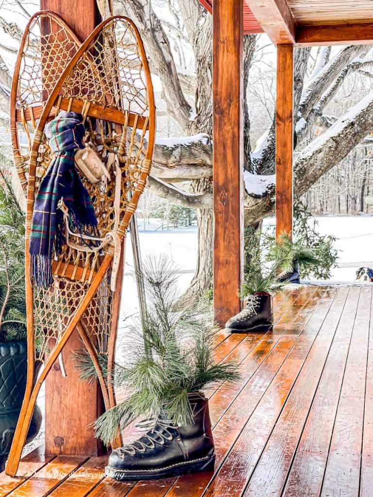 Vintage snows and scarf, vintage ski boots with evergreens on ski house decor styled winter porch in snow.