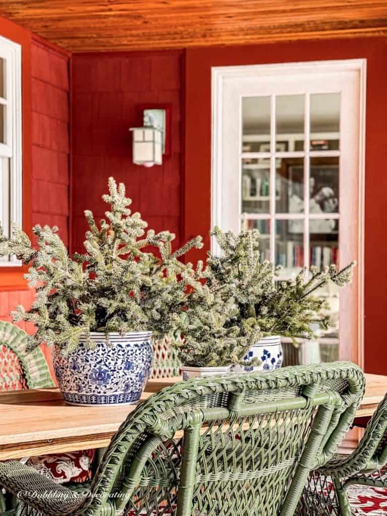 blue and white pots on outdoor porch table with evergreens.  Wicker chairs and red house porch.