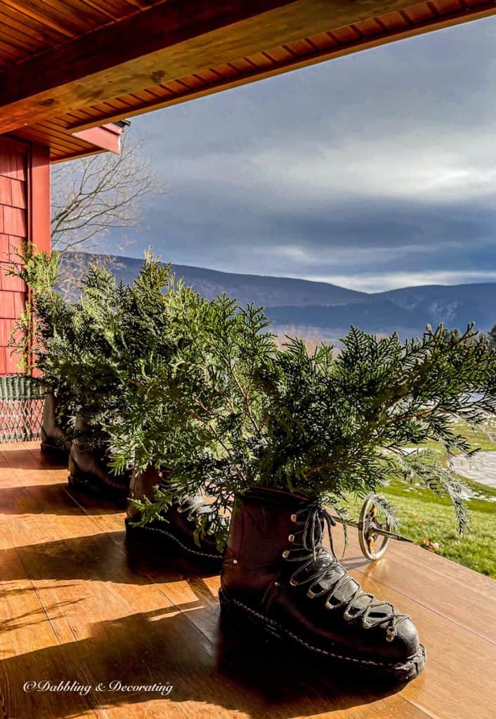 4 old black sport boots lined up on porch table with evergreens on mountain cabin porch.