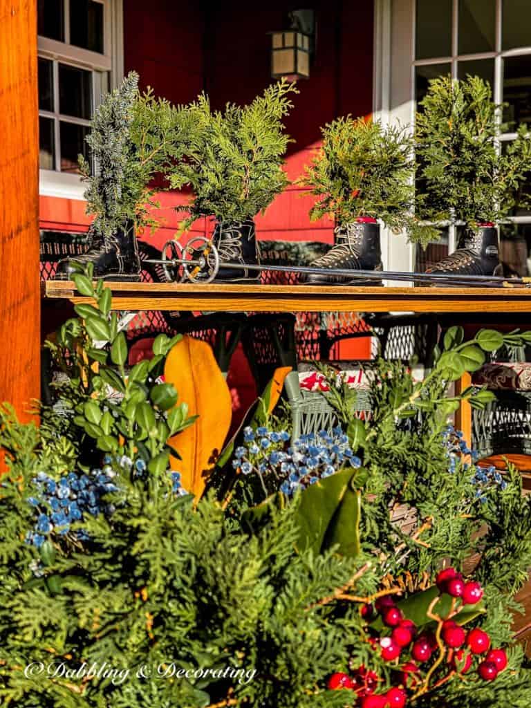 Four old black ski boots with evergreens on ski house decor styled porch.