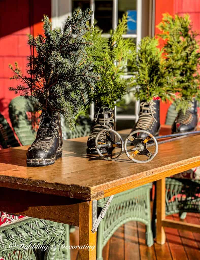 Vintage black ski boots with evergreens on wooden ski house porch table with vintage ski poles in decor.