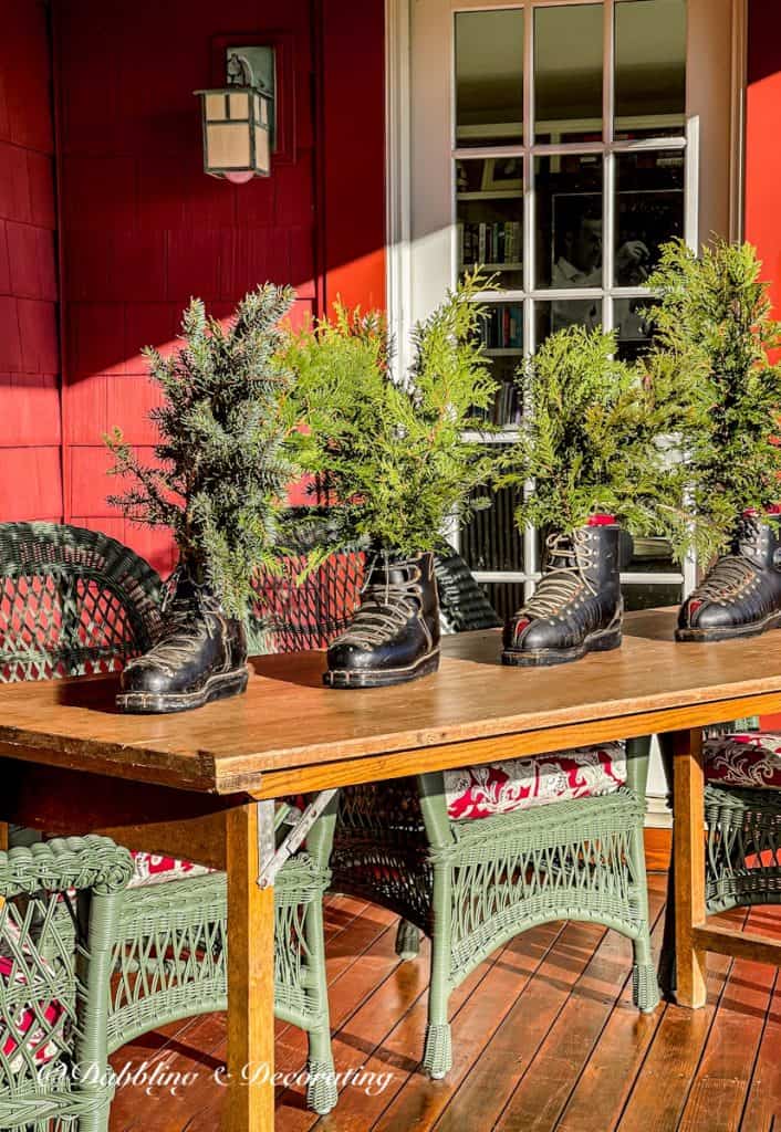 Vintage mens ski boots lined up on wooden ski house porch table with evergreens in Christmas winter decor.