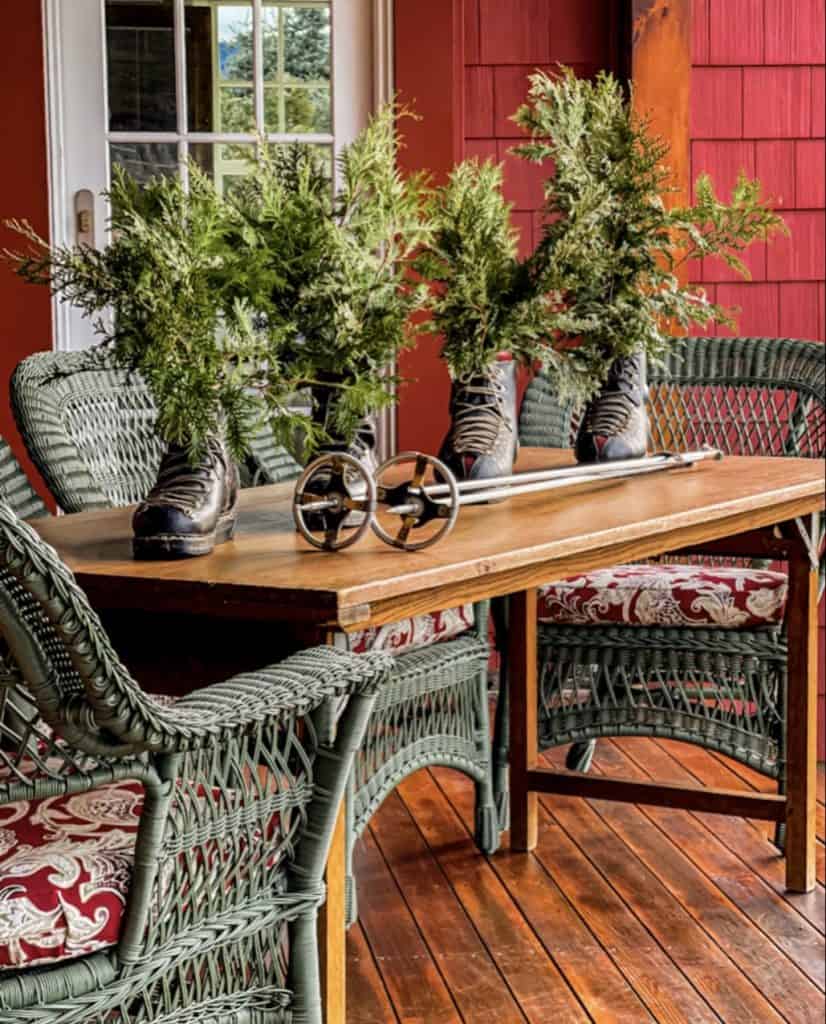 Vintage black ski boots with evergreens and vintage ski poles on wooden table on ski chalet porch decor.