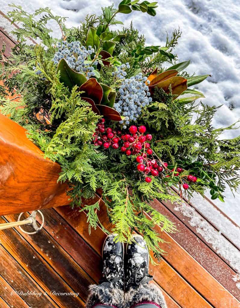 Evergreens, red berries in the snow with boots and vintage ski pole on ski lodge porch steps.