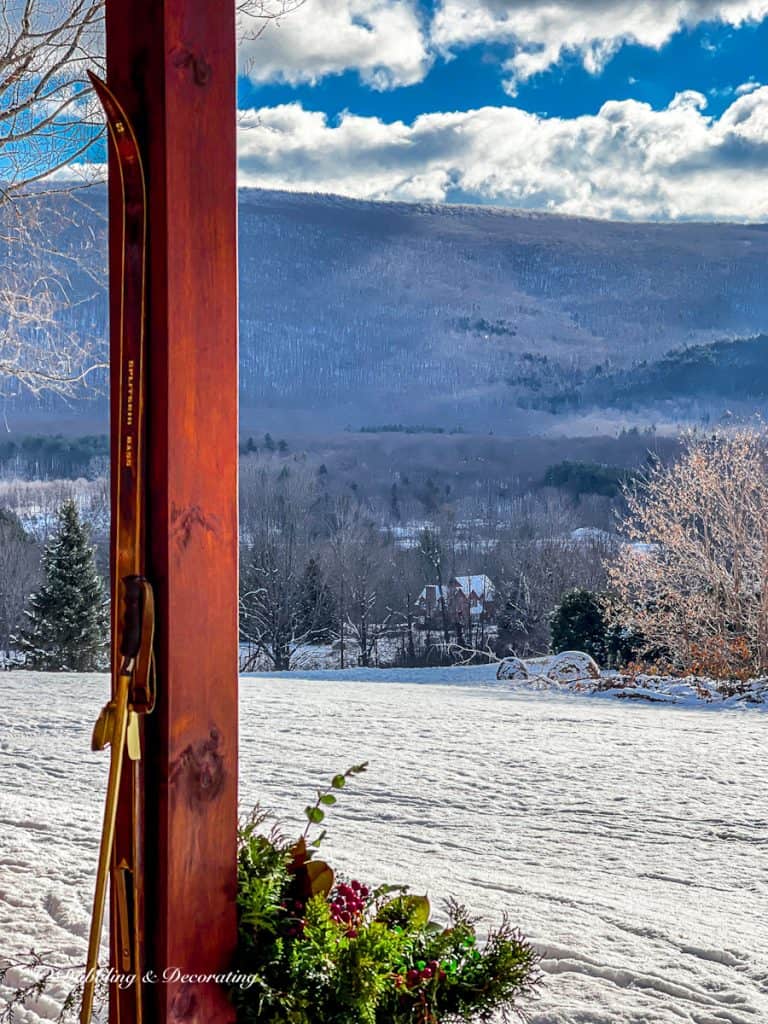 Ski house porch beam with mountain snowy views and vintage skis and poles with evergreen filled urn.