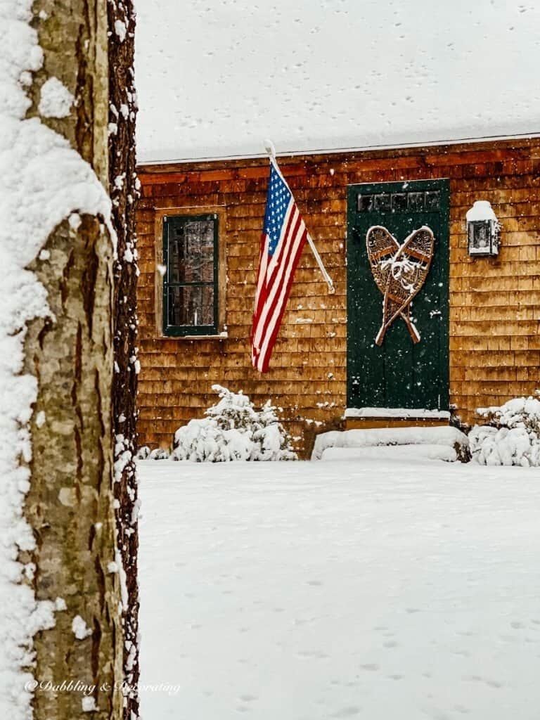 Vintage snowshoes on rustic cedar shakes home in the snow with American flag.