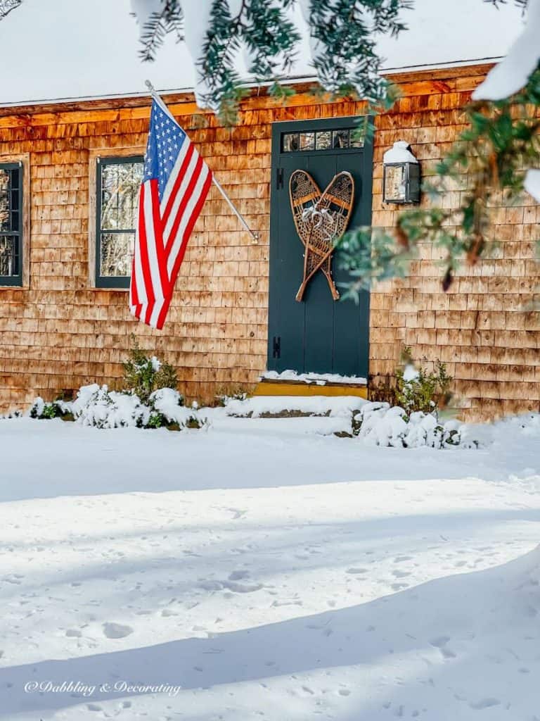 Snowshoes on Essex Green vintage door on rustic cedar shakes home in the snow with American Flag.