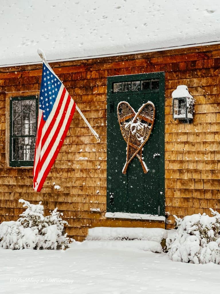 Antique snowshoes on Essex Green vintage door on cedar shakes home during snow storm with American flag flying.