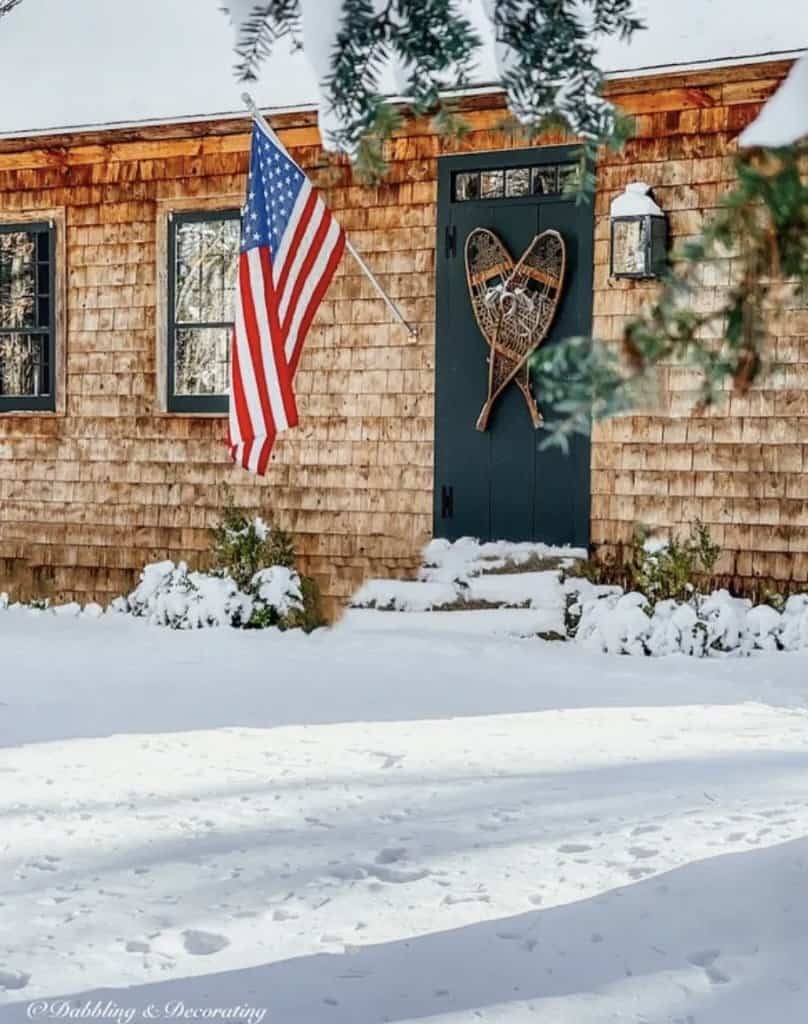 Antique snowshoes on Essex Green vintage door on cedar shakes home in the snow with American Flag.