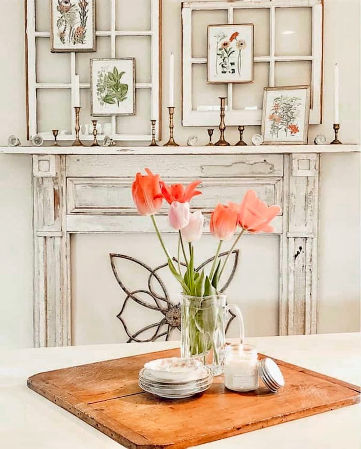 Pink tulips on table in front of faux mantel with botanical wall gallery of frames.